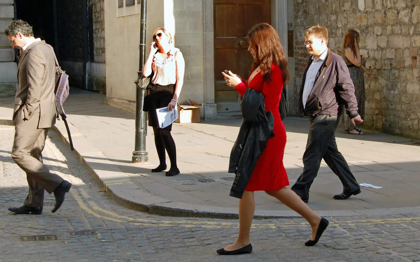 Woman in a red dress walking down a city street while looking at her phone
