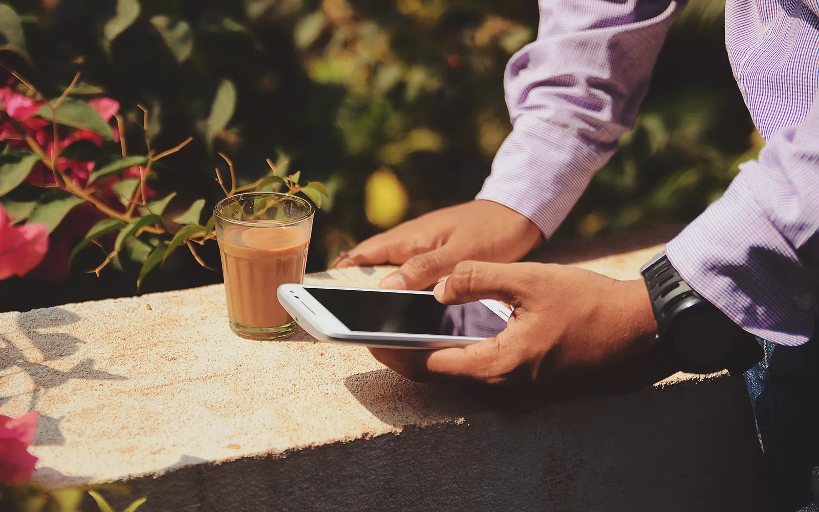 Hands holding a smartphone on a stone ledge beside a glass of tea