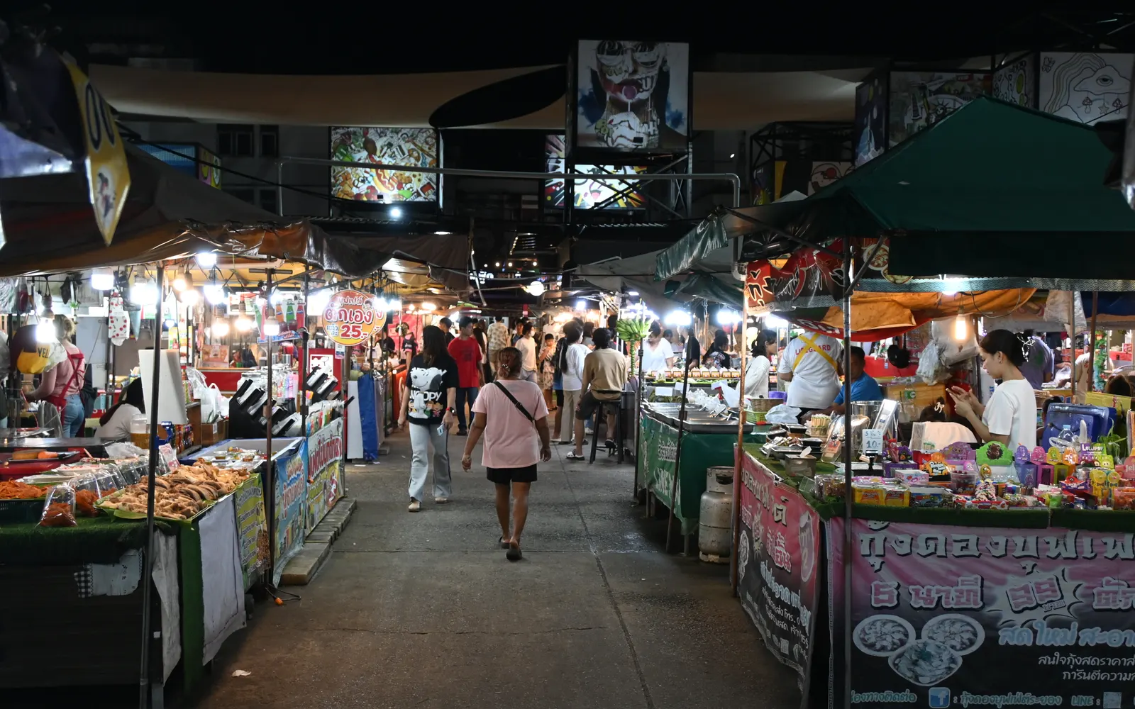 Shoppers walking between brightly lit food stalls at a busy night market