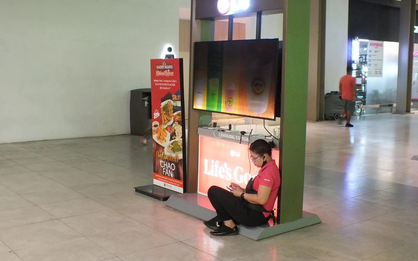 Traveller sitting on the floor using her phone at an airport charging station