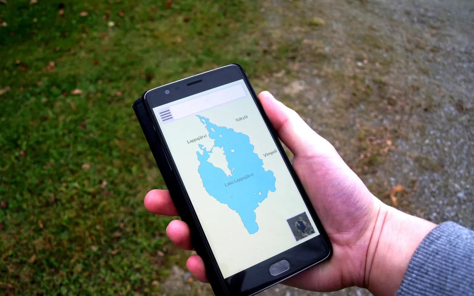 Hand holding a smartphone showing a map, grass in the background