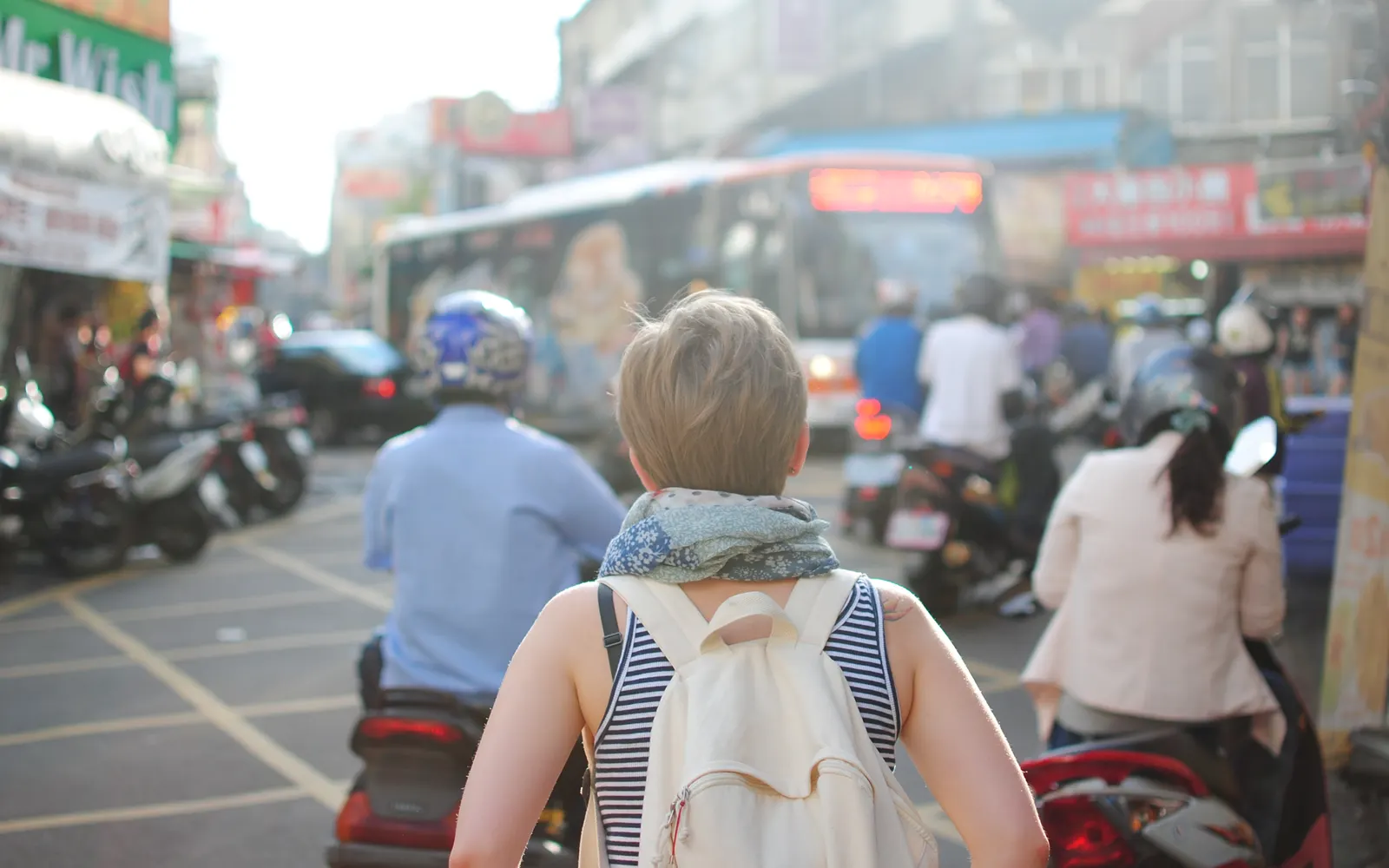 Backpacker walking through busy city traffic with buses and scooters