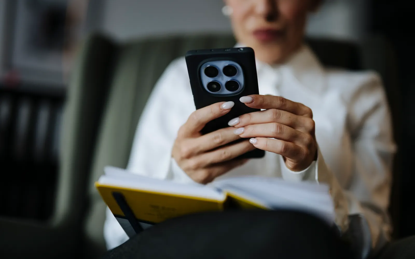 Woman seated holding a smartphone in both hands above an open notebook