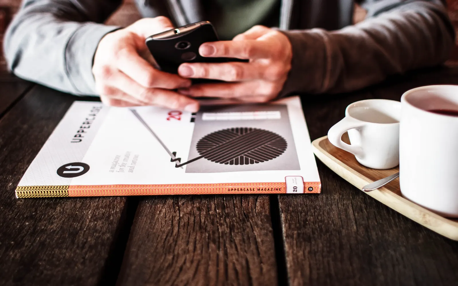 Hands holding a smartphone over a magazine next to a cup of coffee