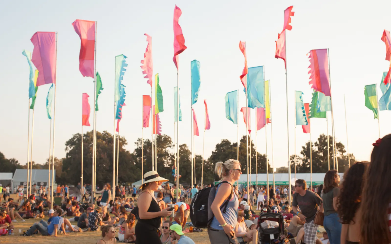 Festival-goers with backpacks walking through a crowded field under colourful flags