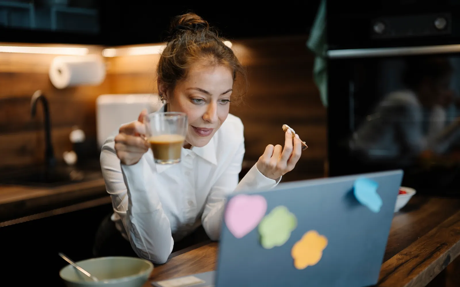 Woman with a coffee glass smiling at her laptop in a kitchen