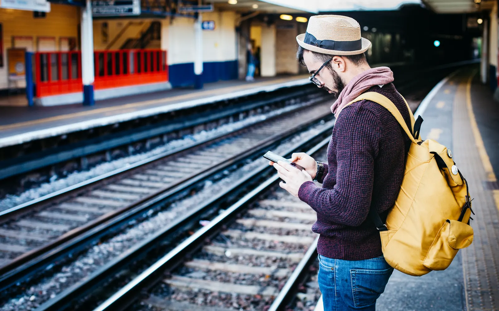 Backpacker in a hat checking his phone on a train station platform