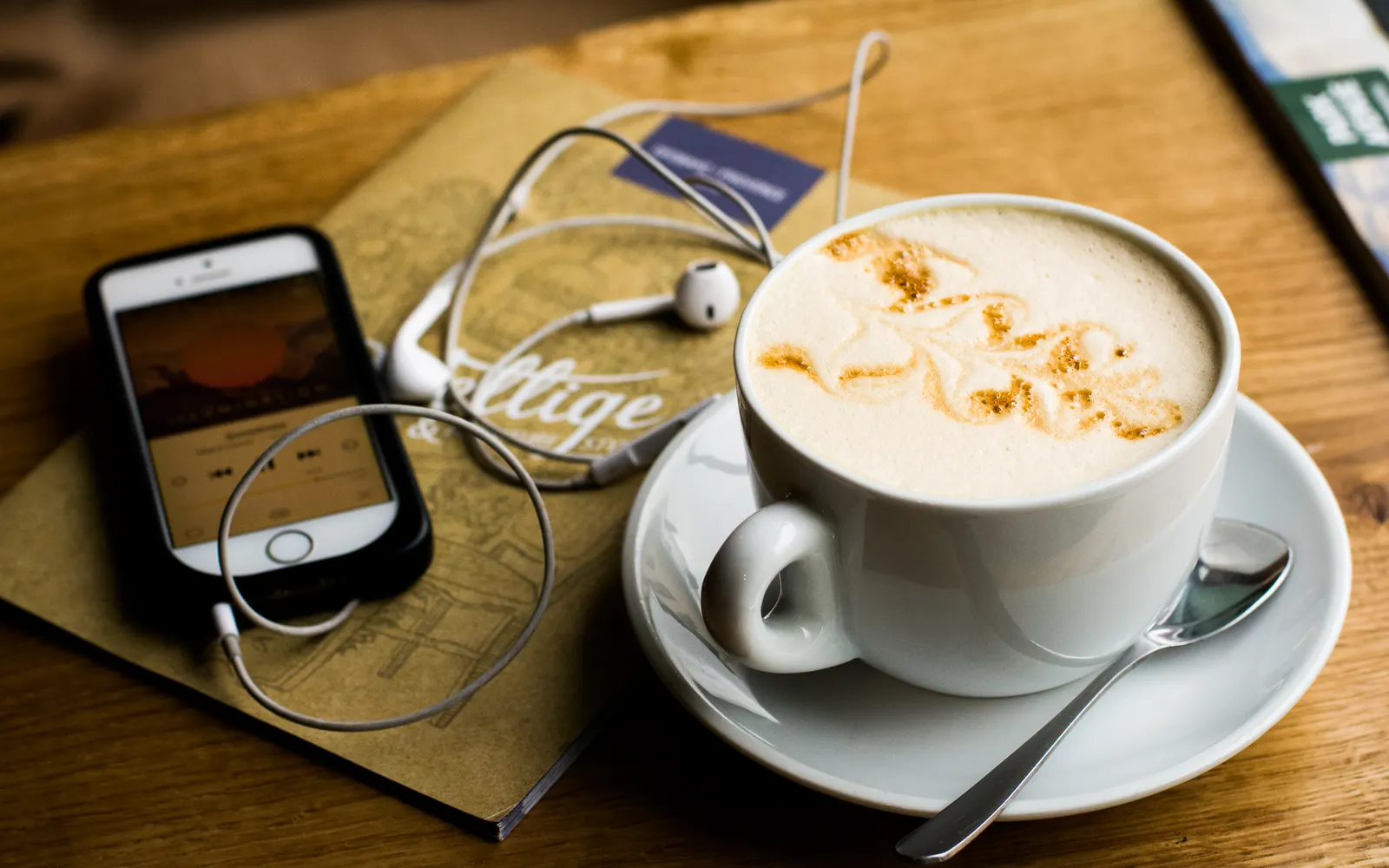 Cappuccino, smartphone and earphones left on a wooden café table